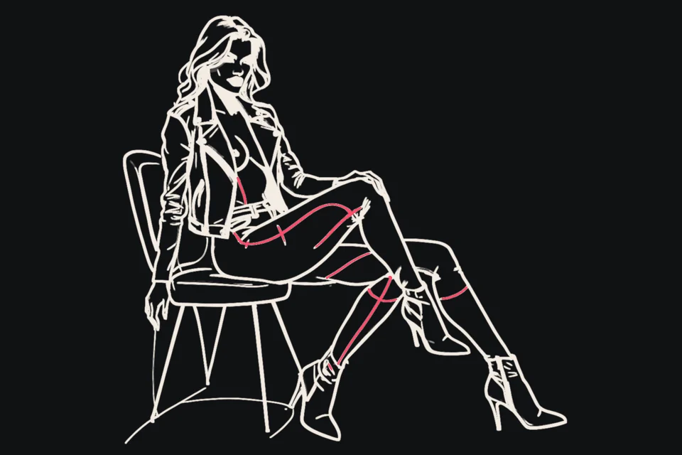 A woman in a leather jacket and boots sits astride a chair